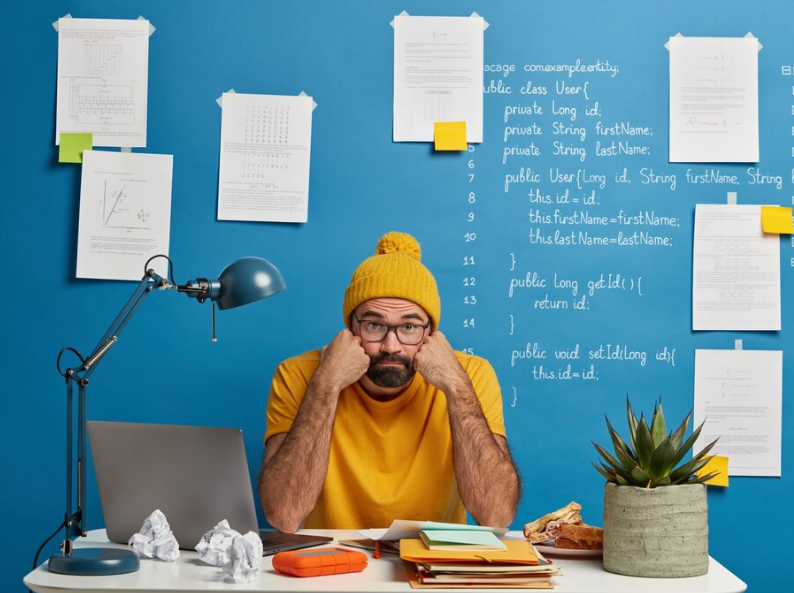 Un étudiant assis à son bureau, entouré de papiers, semblant procrastiné, illustrant le cercle vicieux de la procrastination et du stress académique